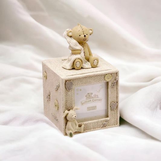 A gorgeous hand painted resin Button Corner cube money box with photo frame. Atop sits an adorable teddy bear figure holding a blanket.